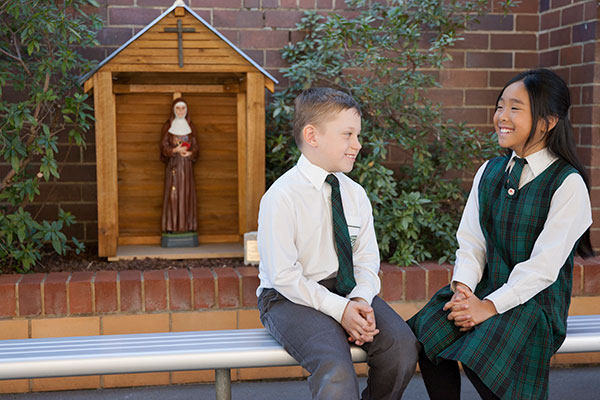 Students sitting on a bench and chatting at St Peter Chanel Catholic Primary School Regents Park